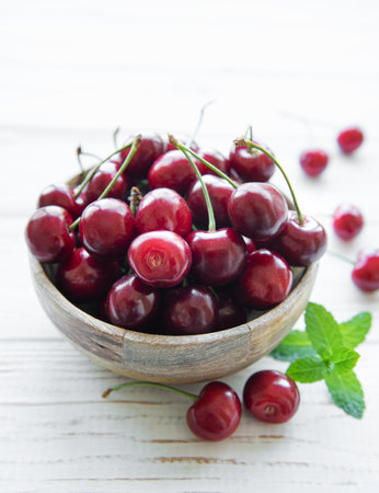 Fresh red cherries fruit in bowl on a white wooden backgroundの写真素材