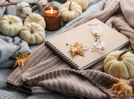 Autumn composition. Cozy home atmosphere with candle, notepad, dry leaves,  decorative pumpkins and knitted sweaterの写真素材
