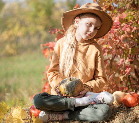 Little girls sitting among hay bales and pumpkins in the autumn gardenの写真素材
