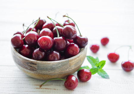 Fresh red cherries fruit in bowl on a white wooden backgroundの写真素材