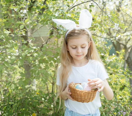 Cute little child wearing bunny ears on Easter day. Girl holding basket with painted eggs.