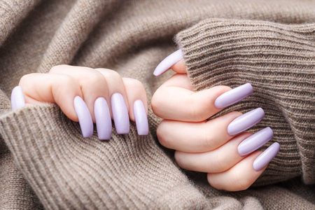 Girl's hands with a soft purple manicure. Background of knitted gray sweater. The concept of beauty, comfort and care.の写真素材