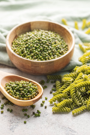 Mung bean fusilli pasta on a gray concrete background. Bowl with raw pasta and green mung bean. Gluten free pasta.の写真素材