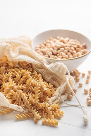 Chickpea ben fusilli pasta on a white tile background. Bag with raw pasta and bowl with chickpea beans. Gluten free pasta.の写真素材