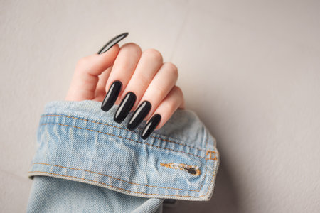 Hand of a young girl wearing a denim jacket with a black manicure on her nailsの写真素材