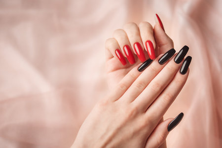 Hands of young girl with red  and black manicure on nails on beige silk  backgroundの写真素材