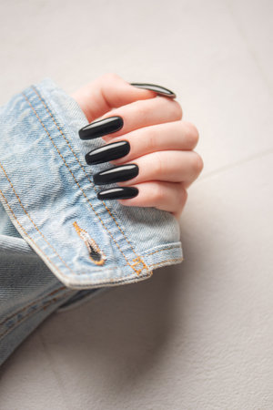 Hand of a young girl wearing a denim jacket with a black manicure on her nails