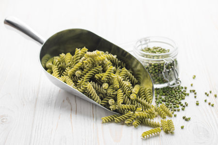 Mung bean fusilli pasta on a wooden background. Scoop with raw pasta and green mung bean. Gluten free pasta.の写真素材