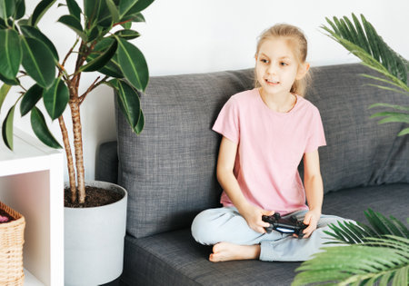 A little girl is playing with a game console at home.の写真素材