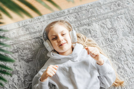Smiling little girl listening music lying on the floorの写真素材