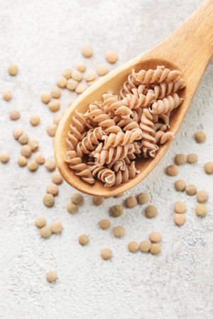 Green lentil fusilli pasta on a gray concrete background. A spoon of raw pasta and green lentils. Gluten-free pasta.の写真素材