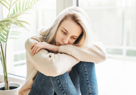 Sad girl near window thinking about something.  Stressed lady feel lonelyの写真素材