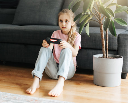 A little girl is playing with a game console at home.の写真素材