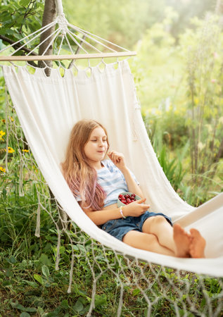 A little girl rests in a hammock and eats cherries in the summer.  Summer in the village.の写真素材