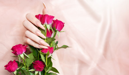 Elegant pastel pink natural manicure. Female hands  with roses on pink silk background.の写真素材