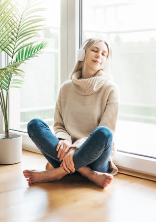 Young blonde woman in headphones listening to music and relaxing at home.の写真素材