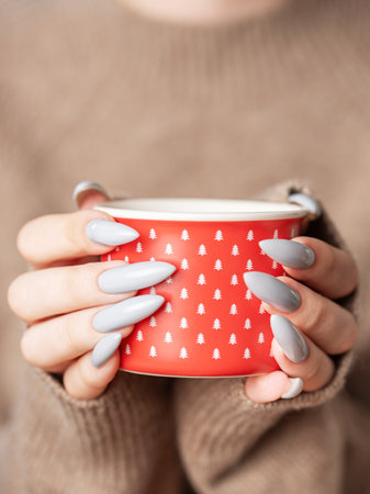 Close up of woman's hand with grey nail polish holding cup of tea or coffeeの写真素材