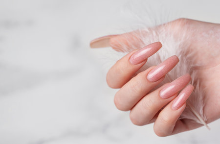 Female hands with pink nail design  hold a feather.  Pink nail polish manicure on marble backgroundの写真素材