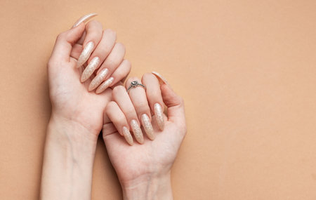 Female Hands on a brown background and beautiful pearl manicure.の写真素材