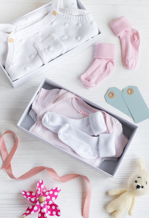 Box with baby stuff and accessories for newborn on white wooden background. Gift box with clothes, socks and knitted toy rabbit. Baby shower concept. Flat lay, top viewの写真素材