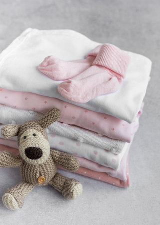 Stack of Baby bodysuits  on a grey background. Baby  crocketed toy of dog  next to a stack rompers for kidsの写真素材