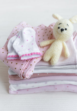 Stack of baby clothes, socks and knitted toy on white wooden backgroundの写真素材