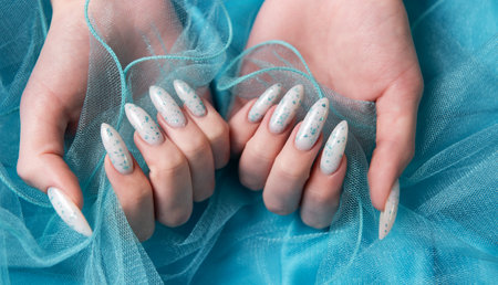 Female hands with blue nail design on blue silk background. Blue nail polish manicure.の写真素材