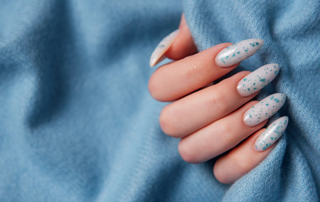 Female hands with blue nail design on blue textile background. Blue nail polish manicure.の写真素材