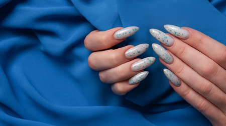 Female hands with blue nail design on blue textile background. Blue nail polish manicure.の写真素材