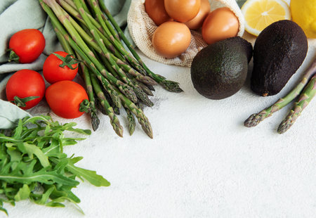A variety of fresh vegetables including asparagus, tomatoes, and arugula are neatly organized...