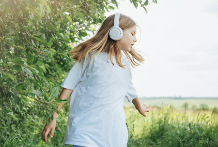 A child  with headphones listening to music and dancing in the park.の写真素材