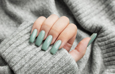 A stylish hand with well-manicured mint-green nails is gently placed on a soft gray sweater, showcasing a fashionable accent in a cozy environment.の写真素材