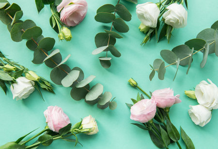 Fresh eucalyptus leaves and pink and white roses are arranged artfully on a bright teal surface,...
