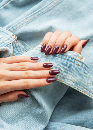Two hands with beautiful burgundy nails delicately placed on a casual denim jacket. The setting highlights a chic and trendy style with a relaxed vibe.の写真素材