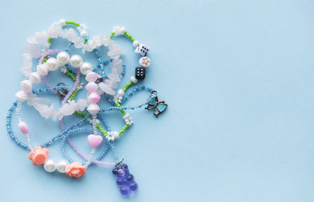 Various beaded necklaces and bracelets in pastel colors are scattered on a light blue surface, highlighting the intricate designs and creativity involved in handmade jewelry.の写真素材