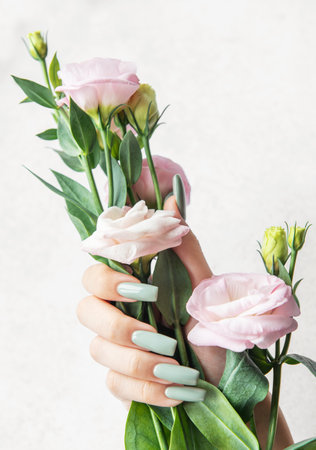 A slender hand showcases long pastel-colored nails while gently grasping a bouquet of soft pink flowers, highlighting a serene and elegant aesthetic.の写真素材