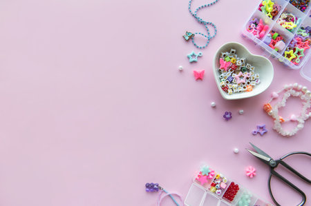 A variety of bright beads, charms, and scissors are arranged on a pink surface, showcasing a fun jewelry-making project with colorful materials and tools.の写真素材