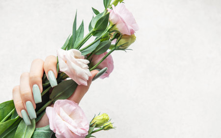 A slender hand showcases long pastel-colored nails while gently grasping a bouquet of soft pink flowers, highlighting a serene and elegant aesthetic.の写真素材