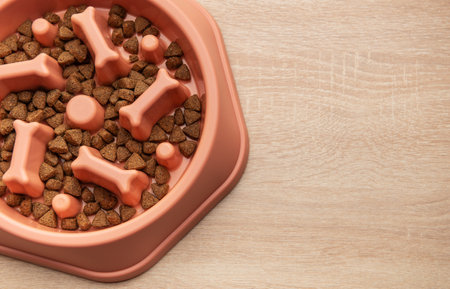 Dry dog food in a slow feeder bowl placed on a wooden surface, promoting healthy eating habits for dogsの写真素材