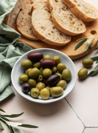 Freshly baked sliced loaf of bread with green and black olives in a bowl, served on a wooden cutting board, perfect for a mediterranean style snack or appetizerの写真素材