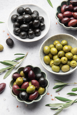 Various olives arranged in bowls with scattered leaves and salt