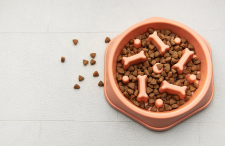 Dry dog food in a pink bowl with bone shapes on a tiled floor