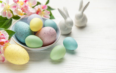 Colorful pastel easter eggs in a bowl with spring flowers and porcelain bunnies celebrating easter...