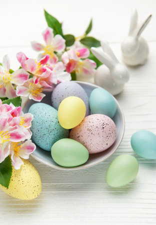 Colorful pastel easter eggs in a bowl with spring flowers and porcelain bunnies celebrating easter...