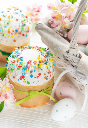 Delicious easter cakes with colorful sprinkles and painted eggs in a basket are surrounded by spring...