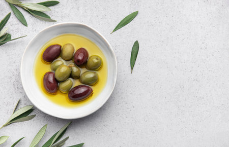 Green and black olives are marinating in a bowl of olive oil, garnished with fresh olive branches, creating a vibrant culinary scene