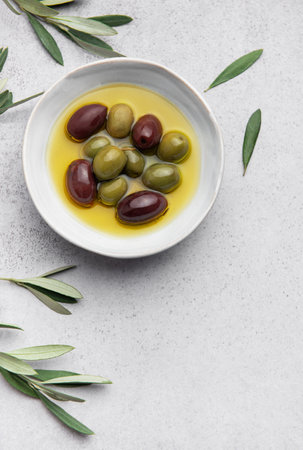 Green and black olives are marinating in a bowl of olive oil, garnished with fresh olive branches, creating a vibrant culinary sceneの写真素材
