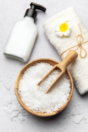 Magnesium bath flakes in wooden bowl with scoop, white towel, and dispenser on grey table creating relaxing spa atmosphereの写真素材