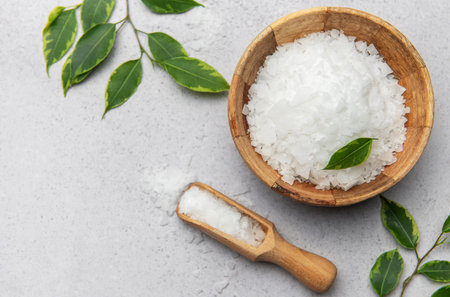 Magnesium chloride flakes in wooden bowl and scoop with green leaves, promoting relaxation and wellnessの写真素材