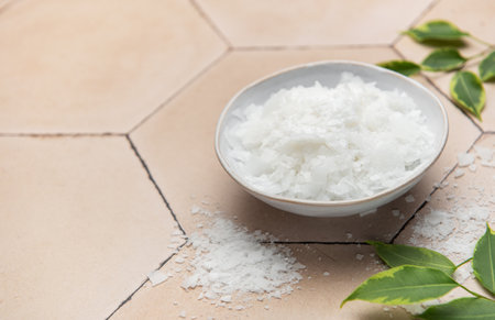 Magnesium chloride flakes in a ceramic bowl, accompanied by green leaves, create a serene spa...